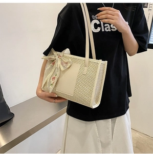 Detail of cream straw tote bag featuring green lace bow and floral embroidery details