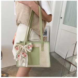 Detail of straw tote bag with floral lace bow and light green leather straps