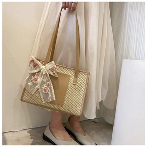 Close-up of a woven straw tote bag with elegant red flower embroidery on a lace bow