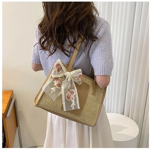 Close-up of woven straw tote bag featuring a white lace bow and pink rose embroidery