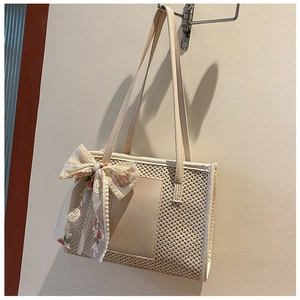 Detail of beige straw shoulder bag with a large floral lace bow and leather handles
