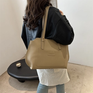Grand sac cabas beige en cuir avec lettrage porté par un mannequin en décor moderne