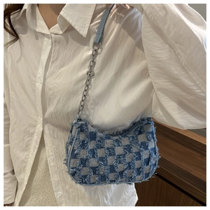 Detail of blue checkerboard denim crescent bag with frayed edges and chain strap