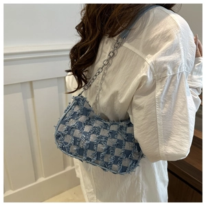 Detail of blue checkerboard denim underarm bag with frayed edges and silver chain strap