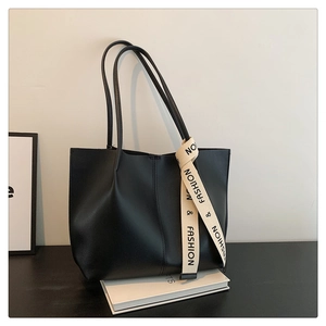 Detailed macro view of the matte black faux leather texture and branded strap on tote bag
