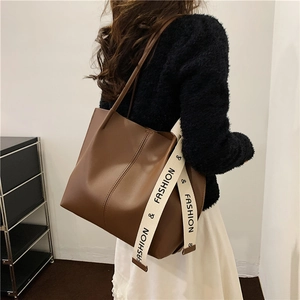 Brown leather tote bag with stylish letter strap shown on shoulder in modern interior