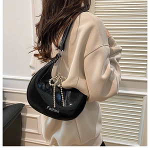 Detail of high-gloss black hobo bag featuring a beaded bow charm and Fashion logo