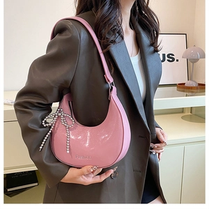 Detailed close-up of a pink crescent shoulder bag with a beaded bow charm and fashion logo