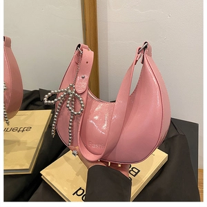 Detail of pink crescent bag with glossy finish, wide strap and silver bow pendant
