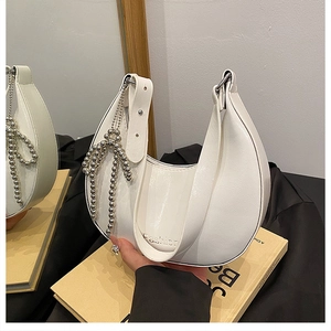 Detail of white leather hobo bag with textured finish and silver beaded bow charm