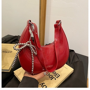 Detail of red patent leather crescent bag with silver beaded bow charm and smooth finish