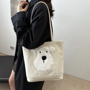 Off-white canvas tote bag with 3D plush puppy patch carried by a model in a black coat