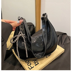 Close-up of black patent leather crescent bag with metallic silver bow charm detail