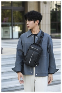 Outdoor shot of men's black nylon chest bag featuring multiple zipper pockets and logo strap