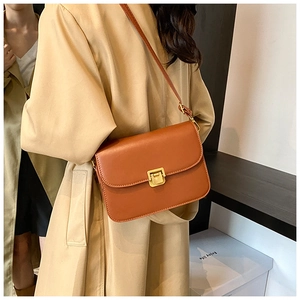 Detail of caramel brown leather shoulder bag with golden buckle on elegant model