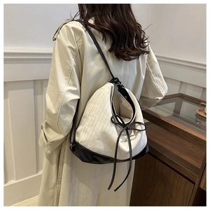 Detail view of canvas backpack with black leather trim worn over a beige trench coat
