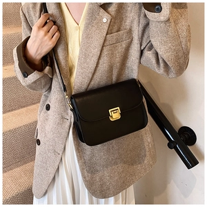 Detail of black leather crossbody bag featuring a gold square buckle and neat stitching