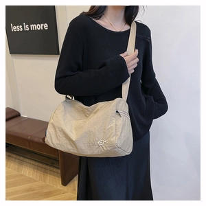 Detail of beige large nylon shoulder bag featuring metal logo and wide woven strap