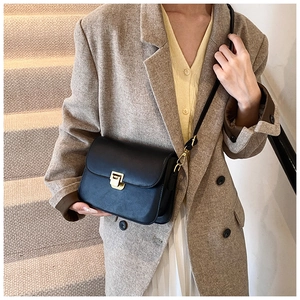 Detail of minimalist black crossbody bag with gold metallic lock on a model outfit