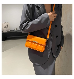 Close-up of bright orange geometric relief bag worn by model over a grey blazer