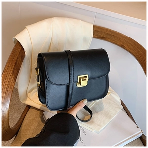 Detail of a black leather crossbody bag featuring a golden buckle against a wooden chair