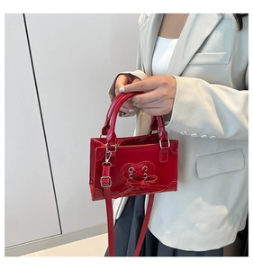 Détail d'un mini sac à main rouge en cuir verni brillant avec nœud en forme de cœur