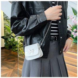Mini white crossbody bag with silver butterfly buckle worn on a black leather jacket