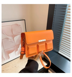 Detail of orange square crossbody bag featuring textured 3D plaid pattern and metal trim