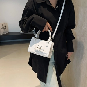 Petit sac à main blanc en cuir avec nœud en cœur porté sur une chemise noire