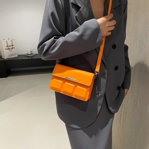 Vibrant orange crossbody bag with 3D chocolate block design worn on grey blazer