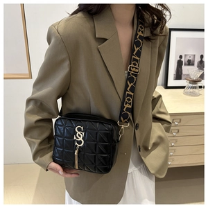 Close-up of black quilted shoulder bag featuring gold S-letter logo and metal tassel detail