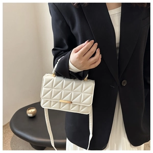 Detail shot of white quilted PU leather handbag with gold rectangular lock and long strap