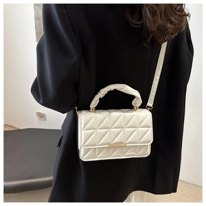 Close-up of white quilted crossbody bag with pleated handle and gold hardware on model