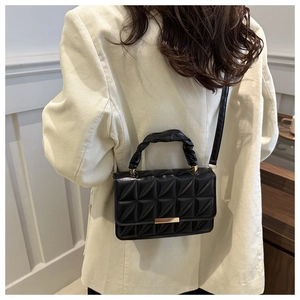 Detail of black quilted crossbody bag with gold buckle on a beige blazer