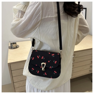 Detail of crossbody bag with cherry print, gold horseshoe buckle, and leather strap