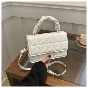 Close-up of a white quilted crossbody bag with gold buckle and a soft scrunched handle