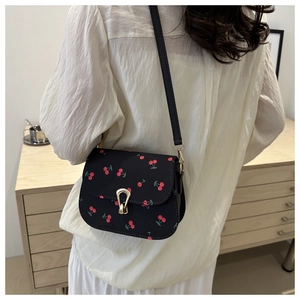 Detail showing black crossbody bag with red cherry prints and golden metal clasp