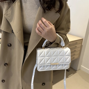 White quilted crossbody bag with geometric patterns and gold accents on a khaki coat