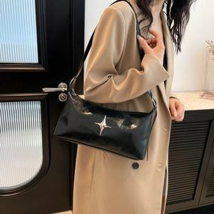 Large black patent leather shoulder bag with silver star charm worn by a model in a suit