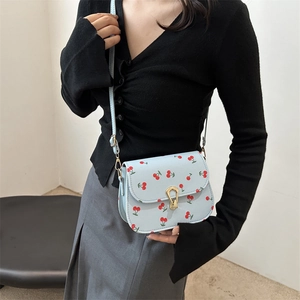 Light blue crossbody square bag with cherry print and golden metal clasp on a model