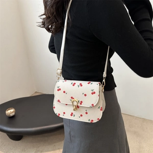 White cherry print crossbody bag with gold teardrop latch on a crossbody strap