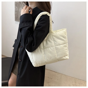 Close-up of a white quilted tote bag worn over the shoulder with a black trench coat