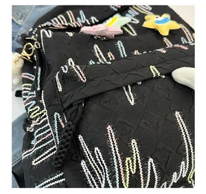 Close-up of black quilted backpack fabric with colorful stitching and star plush charm
