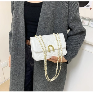 Detail of white quilted crossbody bag with golden U-shaped ball lock and chain strap