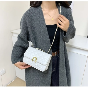 Detail showing white quilted crossbody bag with gold horseshoe clasp and chain strap