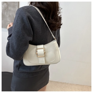 Detail of white patent leather underarm bag with gold buckle on shoulder of a model