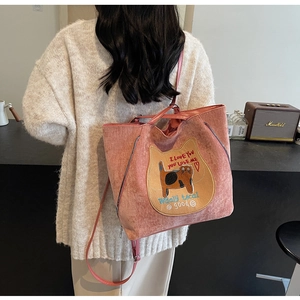 Detail of pink corduroy tote bag with cat embroidery worn by model in a cozy indoor setting