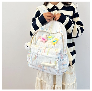 Detail of white backpack with textured embroidery and cute smiling star plush pendants