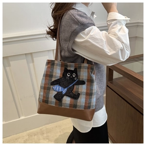Détail du sac cabas en laine à carreaux avec un patch chat noir et bordure cuir