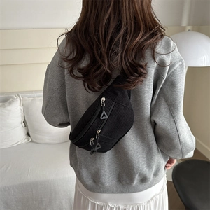Back view of black corduroy crossbody bag worn by a model in a minimalist home setting